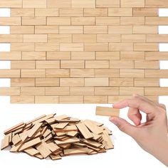 a hand holding a wooden block next to a pile of wood planks on a white surface