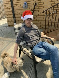 a man in a santa hat sitting on a chair next to a small dog with his head down