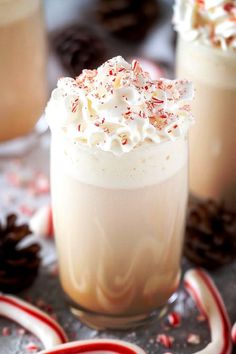 two glasses filled with hot chocolate and whipped cream on top of peppermint sprinkles