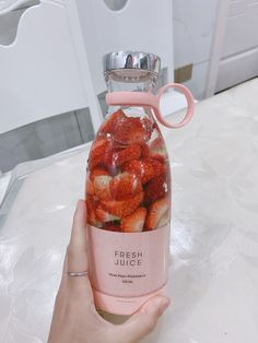 a person holding up a jar filled with strawberries on top of a white table