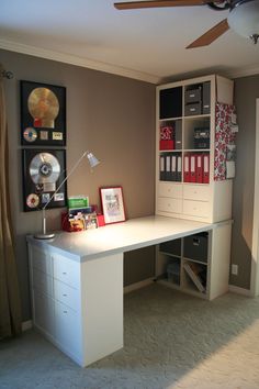 a white desk sitting under a ceiling fan next to a wall mounted book shelf with cd's on it