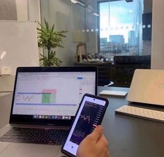 someone is using their cell phone while sitting at a desk in front of two laptops