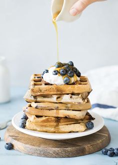 a stack of blueberry waffles with syrup being drizzled on top