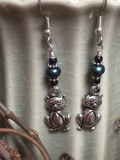 This set of pudgy belly cats will dangle from your ears with cuteness! Wear them as casual everyday jewelry. You will get tons of compliments.Earrings are made using surgical steel ear wires. I use wrapped loops to give a finished look. Earrings come with rubber ear backs that slide on to keep earrings from falling out of ears.Color: silver, dark grey pearl, iris purpleEarrings length: see pictureTO SEE MORE BEADED EARRINGS CLICK HEREORDERS PROCESS AND SHIP IN 1-5 BUSINESS DAYS. Large orders cou Cute Adjustable Cat Design Earrings, Adjustable Cute Cat Design Earrings, Nickel-free Cat Ears Jewelry For Gifts, Cute Cat Design Adjustable Earrings, Nickel-free Cat Ears Jewelry Gift, Handmade Silver Cat Ears Jewelry, Cute Cat Design Dangle Jewelry, Cute Handmade Cat Ears Jewelry, Cat Design Metal Drop Earrings