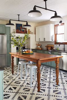 a kitchen with white cabinets and black and white floor tiles on the floor, along with an island table surrounded by stools