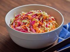 a white bowl filled with coleslaw on top of a wooden table next to chopsticks