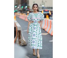 a woman is walking down the street wearing a white and green dress with flowers on it