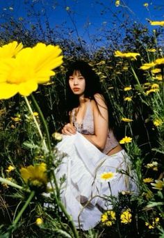 a woman is sitting in the middle of a field with yellow flowers and daisies