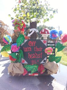 a sign that says off with their heads on the back of a truck decorated with paper flowers and leaves