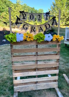 a wooden crate filled with flowers on top of a grass covered field next to a sign that says grad