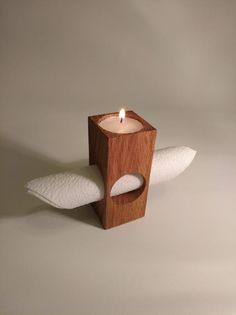 a wooden candle holder with two white pillows on the bottom, and a lit candle in the middle