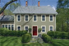 a blue house with white trim and red door in the middle of a green yard