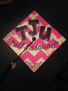 a pink and gold graduation cap with the word tu in black letters on it, sitting on top of a table