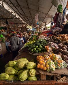 an open air market with lots of fruits and vegetables on the table, people shopping in the background