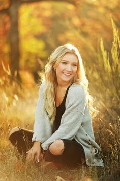 a woman is sitting in the grass and smiling at the camera with her hands on her knees