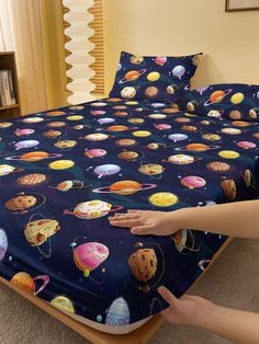 the bed is covered with an image of planets and stars on it, as well as a hand reaching for something