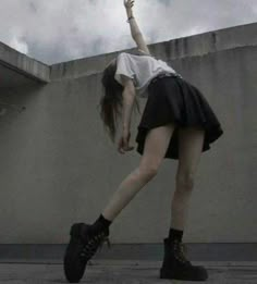 a woman in black and white is reaching up into the air with her hand while standing on concrete