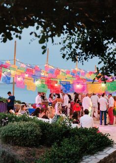 a group of people standing around each other in front of a building with colorful lights hanging from it