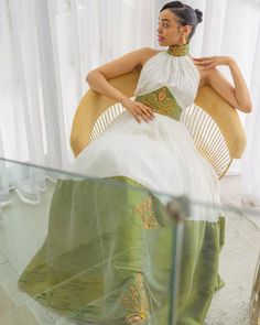 a woman sitting in a chair wearing a green and white dress with gold embroidery on it