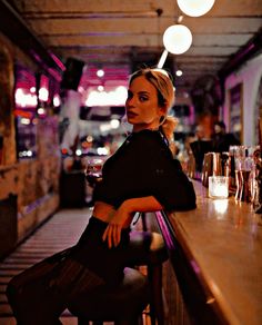 a woman sitting at a bar with her arms on the back of a wooden bench