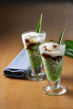 two glasses filled with dessert sitting on top of a wooden table