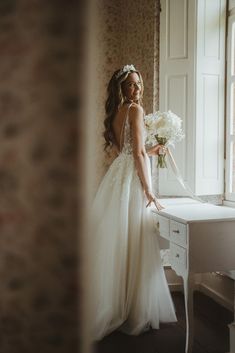 a woman standing in front of a window next to a table with flowers on it