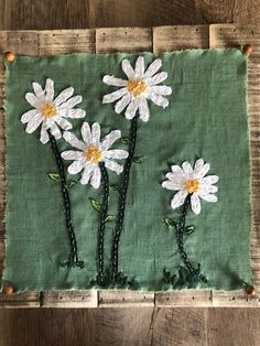 three white daisies are on a green piece of cloth