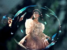 a woman in a white dress is standing inside a glass ball with bubbles floating around her