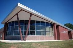 the building is red and white with many windows on it's sides, along with grass and trees