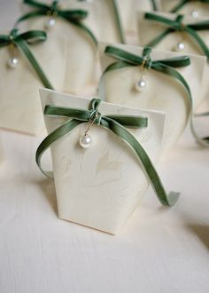 four white heart shaped boxes with green ribbons tied around the top and bottom, each containing a single pearl ornament