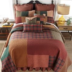 a bed with plaid comforter and pillows in a room next to a lamp on a table