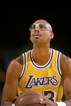 a man holding a basketball in his right hand and wearing sunglasses on top of it