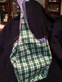 a green and white plaid bag hanging on a black cloth covered chair with a purple ribbon