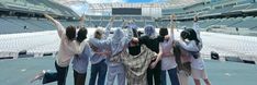 four women standing in front of an empty stadium bleachers with their hands up