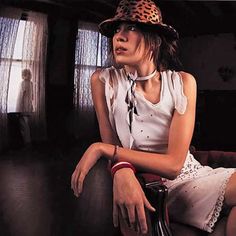 a woman sitting on top of a chair wearing a leopard print hat and white dress