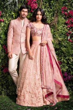 a man and woman standing next to each other in front of some bushes with pink flowers