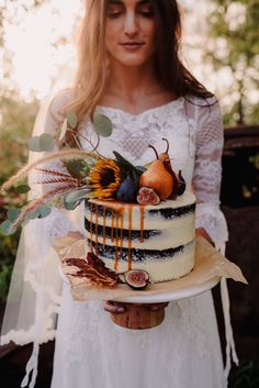 a woman holding a cake decorated with fruit and flowers on top of a wooden board