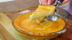 a person cutting into a pie in a glass dish on a wooden table with a knife