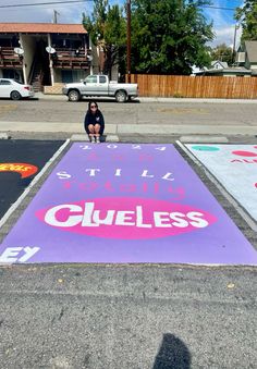 a woman sitting on the side of a parking lot next to a sign that says guess