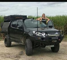 a woman standing next to a black truck in the middle of a field with corn