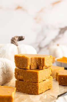 pumpkin fudge bars stacked on top of each other next to some white pumpkins