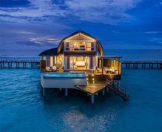 a house on stilts in the ocean with a swimming pool and hot tub at night