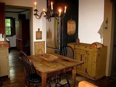 an old fashioned dining room table and chairs with candles on the chandelier above it