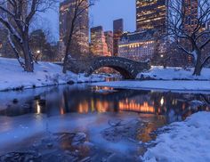 a bridge over a small stream in the middle of a snow covered park at night