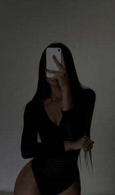 a woman in a black bodysuit taking a selfie with her cell phone while sitting on a bed