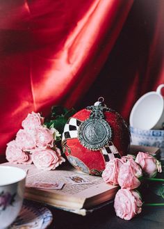 a table topped with pink roses next to a cup and saucer on top of a book