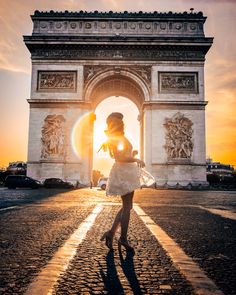 a woman is standing in front of the arc de trioe triumph gate at sunset