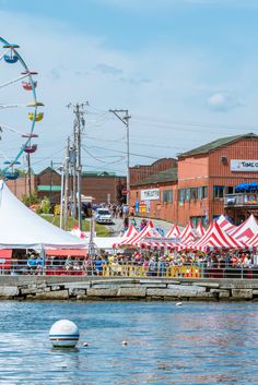 an amusement park next to the water with ferris wheel and tents in the foreground