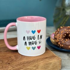 a pink and white coffee mug sitting on top of a wooden table next to a donut