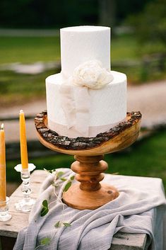 a three tiered white cake sitting on top of a wooden table next to candles